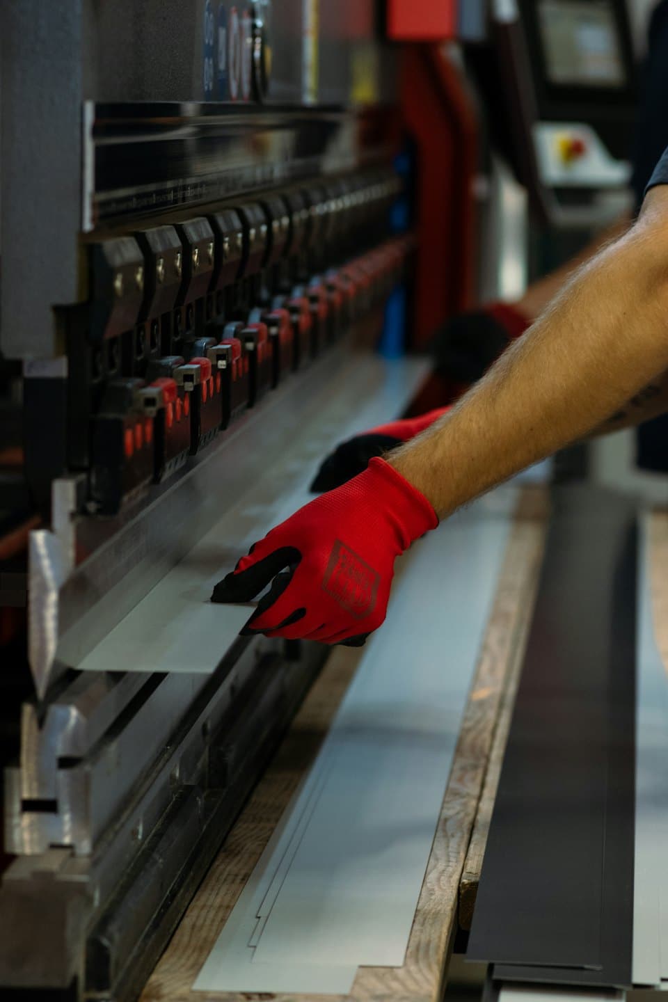 Worker in red gloves operates a press brake machine with sheet metal.
